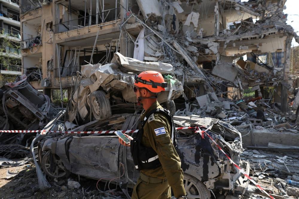 Rescue personnel walks past damaged vehicles at an impact site following missile attack from Iran on Israel, in Ramat Gan, Israel, on Saturday. REUTERS