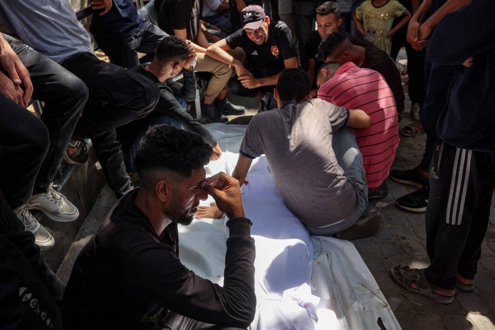 Mourners sit by the body of a person who was killed following reported Israeli attacks on aid queues in the Sudaniya area in northwestern Gaza, during the funeral at Al-Shifa hospital in Gaza City on Saturday. AFP