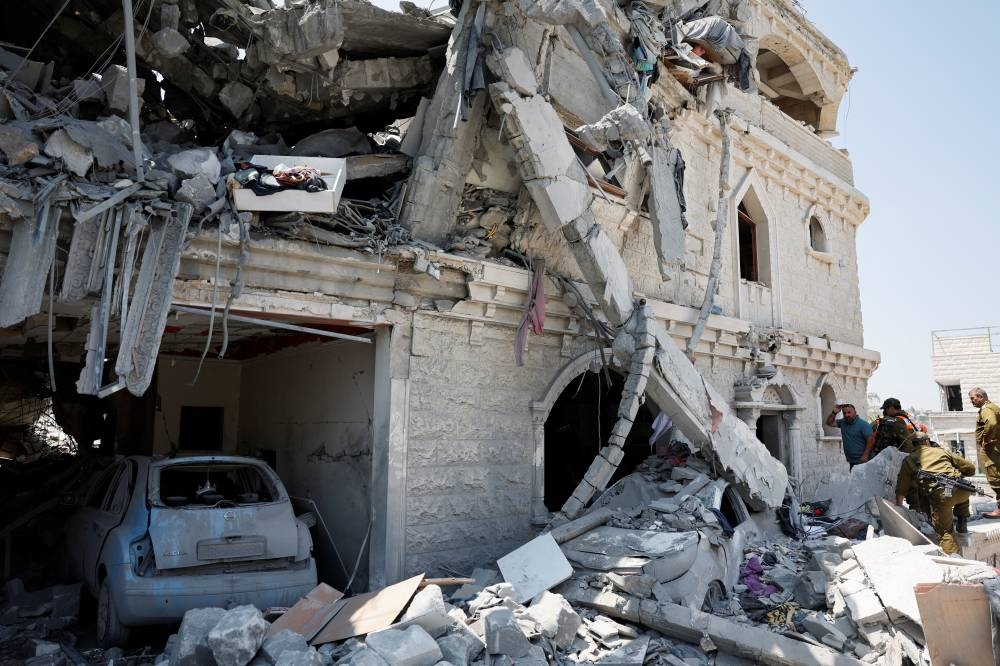 People including Israeli soldier stand next to debris and a damaged vehicle after missiles fired from Iran impacted a residential building, in Tamra, northern Israel, on Sunday. REUTERS