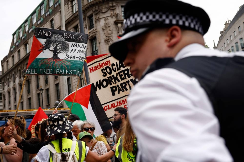 A MET police officers stands in front of protesters waving Palestinian a flags and holding placards as they take part in a march through central London, on Saturday, at a demonstration organised by the Palestinian Solidarity Campaign. AFP