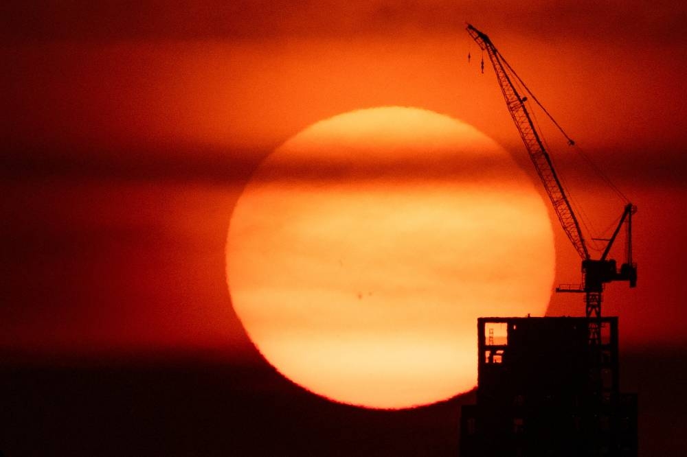 The sun sets behind a crane in Manhattan as an extreme heat warning is in effect in New York City. (Reuters)