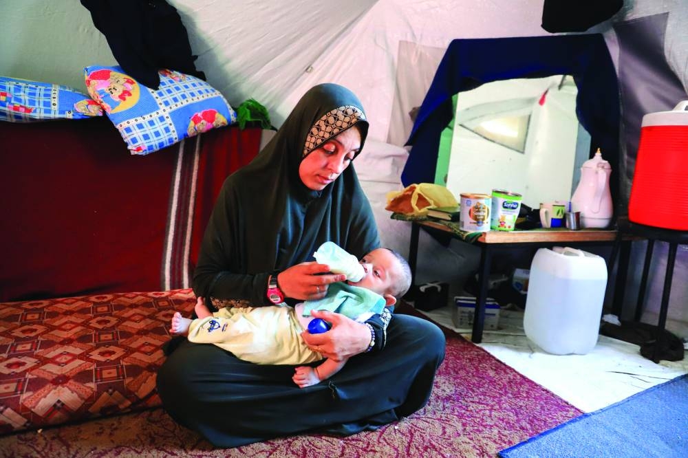 
Displaced Palestinian woman Fatmeh Jundieh sits inside a tent, holding one of her two-month-old twins, as she struggles to find formula milk and diapers amid ongoing shortages, in Gaza City. 