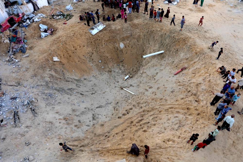 Palestinians gather around a huge crater after the Israeli army targeted the tents of displaced people in the northern Al-Rimal neighborhood of Gaza City on Saturday. AFP