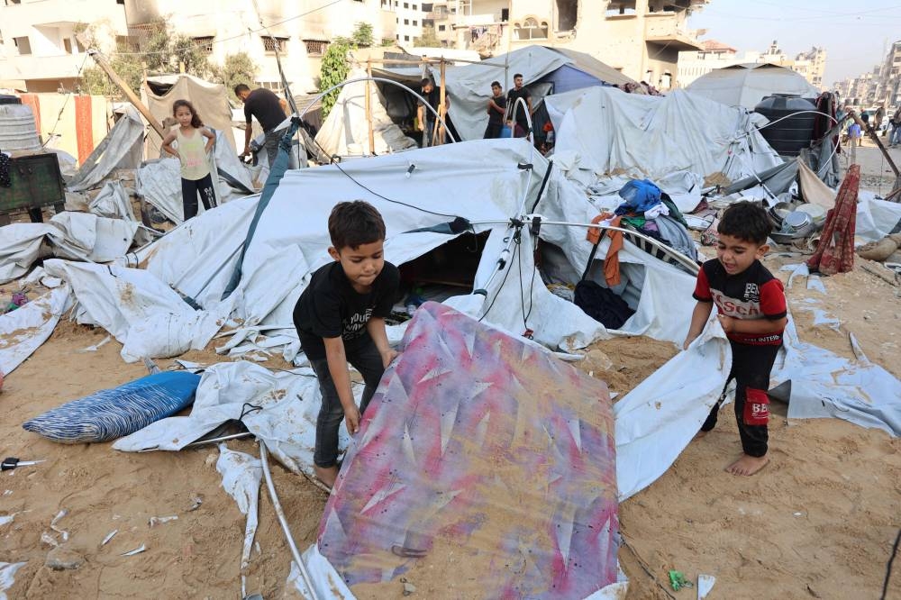 Palestinian little children lift a sand covered mattress after the Israeli army targeted the tents of displaced people in the northern Al-Rimal neighborhood of Gaza City on Saturday. AFP