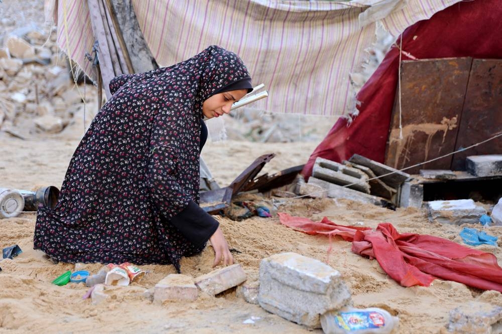 A Palestinian woman searches for an item in the sand after the Israeli army targeted the tents of displaced people in the northern Al-Rimal neighborhood of Gaza City on Saturday. AFP