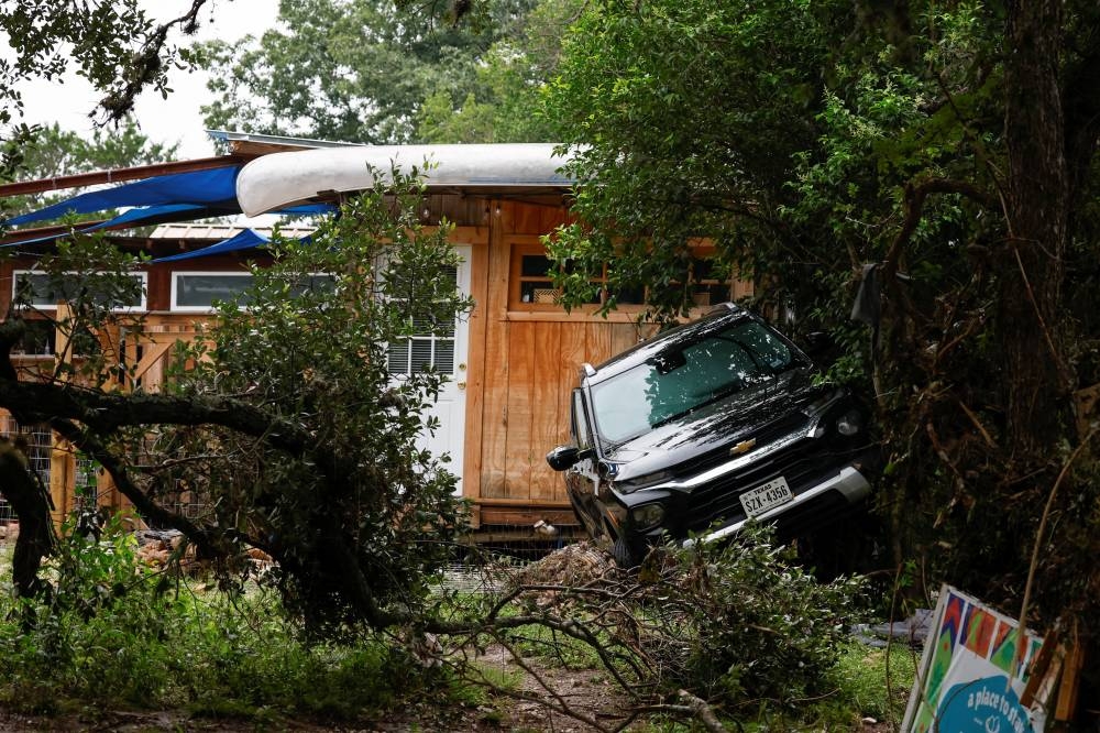 A vehicle rests against vegetation near a cabin, following flash flooding, in Hunt, Texas, on Sunday. REUTERS