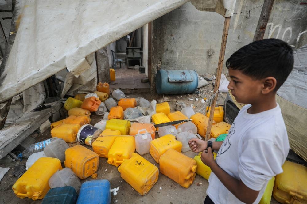 A Palestinian boy inspects the site of an Israeli strike that killed Palestinians, gathered to collect water from a distribution point, in Nuseirat in the central Gaza Strip, on Sunday. REUTERS