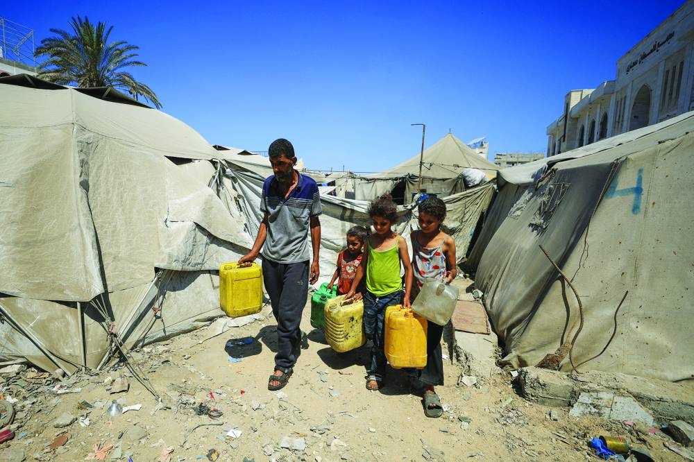 
Displaced Palestinian man Akram al-Manasra and his children make their way to collect water from a distribution point amid shortages, in Gaza City, yesterday. 