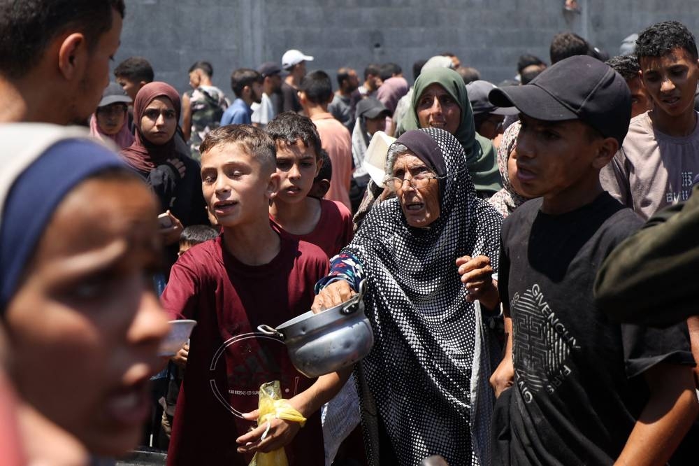 An elderly woman holds out an empty pot at a food distribution point in the Nuseirat refugee camp in the central Gaza Strip Saturday 