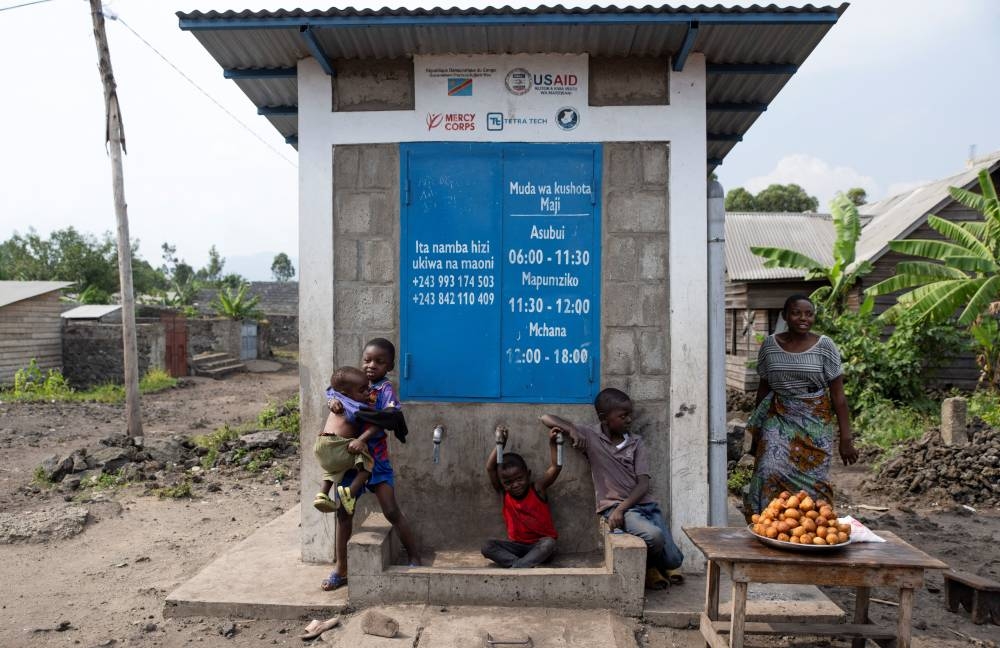 Children play in front of a non-operational standpipe kiosk that was supposed to be supplied by the water reservoir, where incomplete water connections caused by USAID funding cuts to the NGO Mercy Corps have led to ongoing water shortages, in Goma, North Kivu province, Democratic Republic of Congo.