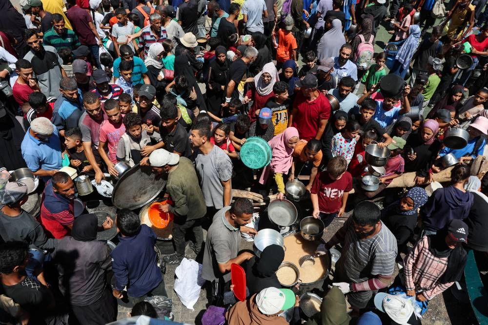Palestinians gather to receive food from a charity kitchen in Nuseirat, central Gaza Strip, Sunday 