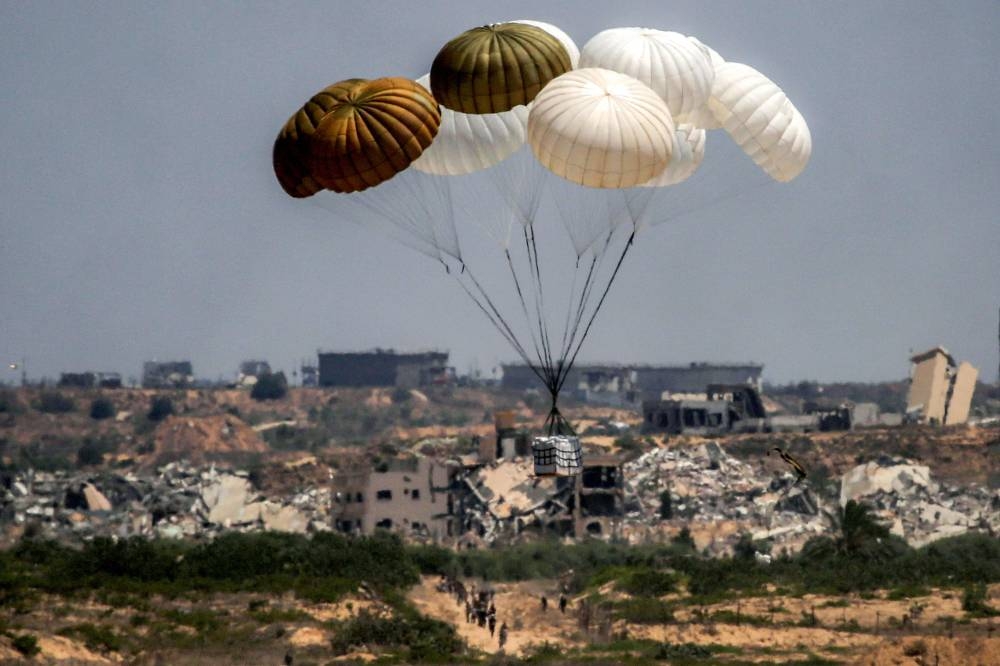 Palestinians rush to the scene as aid pallets are parachuted after being dropped from a military plane over Nuseirat in the central Gaza Strip Tuesday.