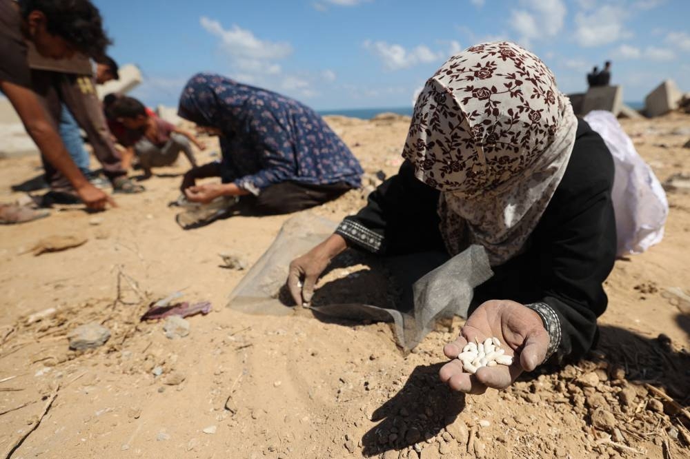 Palestinian women search the sand for legumes or rice in Nuseirat in the central Gaza Strip Tuesday.