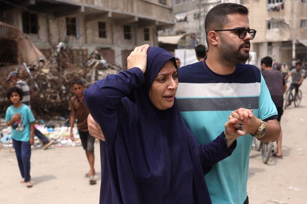 A Palestinian man helps a wounded woman flee the site of an Israeli strike west of Gaza City on August 12, 2025. (AFP)
