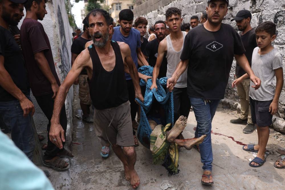 People recover the body of a Palestinian man, killed in an Israeli strike, west of Gaza City on August 12, 2025. (AFP)