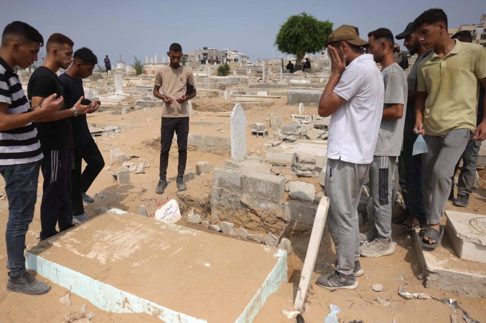 Palestinians recite the Fatiha over the grave of Al Jazeera correspondent Anas al-Sharif, who was killed alongside other journalists in an Israeli strike, at a cemetery in Gaza City on August 12, 2025.(AFP)