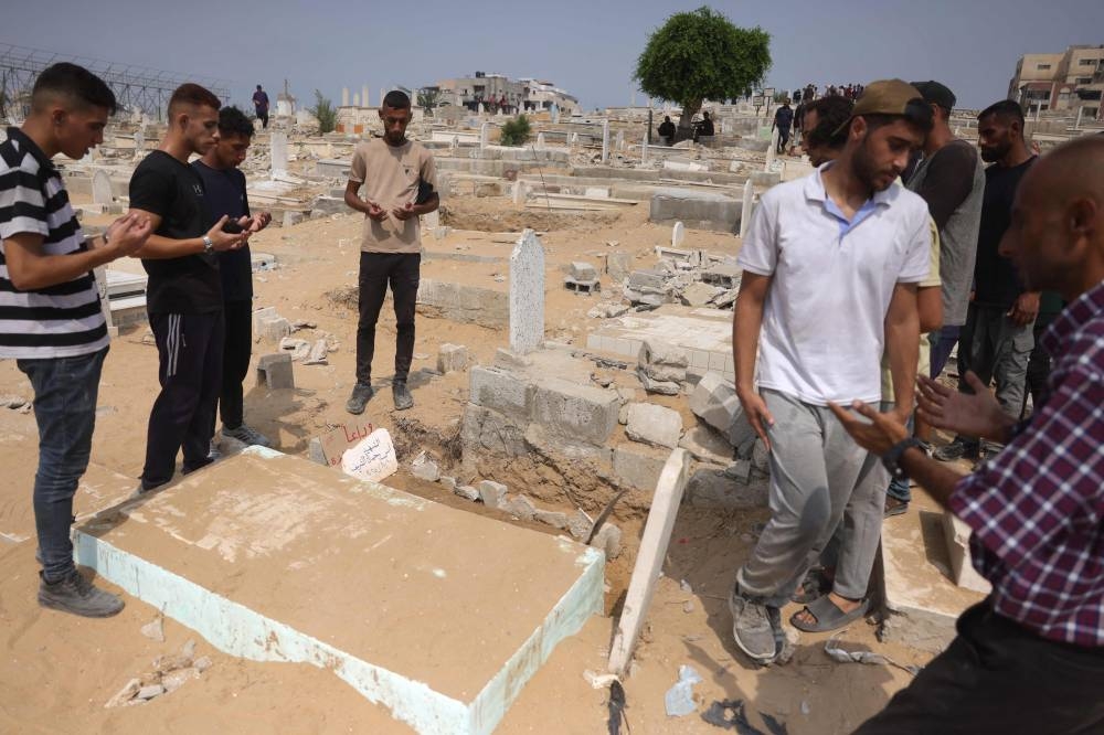 Palestinians recite the Fatiha over the grave of Al Jazeera correspondent Anas al-Sharif, who was killed alongside other journalists in an Israeli strike, at a cemetery in Gaza City on August 12, 2025. (AFP)