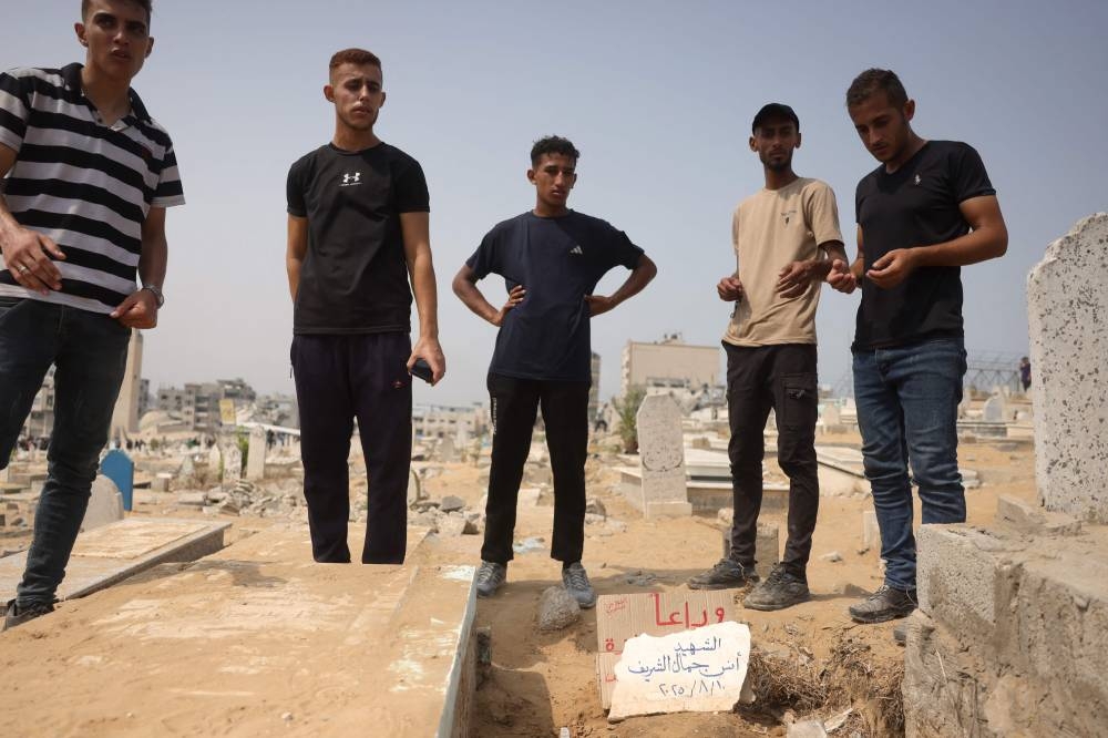Palestinians recite the Fatiha over the grave of Al Jazeera correspondent Anas al-Sharif, who was killed alongside other journalists in an Israeli strike, at a cemetery in Gaza City on August 12, 2025. (AFP)