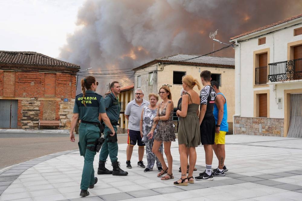 Members of Spain's Civil Guards accompany people waiting to be evacuated in Losacio, north of Zamora, on August 12, 2025. A man died from burns and thousands of people were forced to evacuate as wildfires swept through parts of Spain Tuesday, fueled by strong winds and a searing heat wave that has gripped the country for 10 days.(AFP)