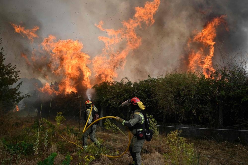 A firefighter falls on the ground while working to extinguish a wildfire in San Cibrao das Viñas, outside Ourense, northwestern Spain, on August 12, 2025. A man died from burns and thousands of people were forced to evacuate as wildfires swept through parts of Spain Tuesday. (AFP)