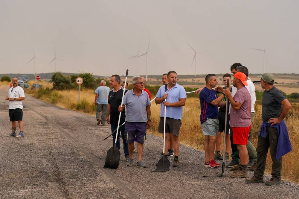 Residents stand with shovels ready to assist in extinguishing a wildfire near Losacio, north of Zamora, on August 12, 2025. A man died from burns and thousands of people were forced to evacuate as wildfires swept through parts of Spain, fueled by strong winds and a searing heat wave that has gripped the country for 10 days. (AFP)
