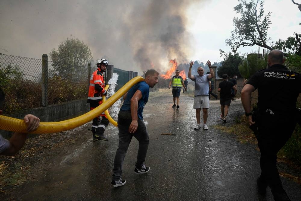 Civilians, firefighters and police work to extinguish a wildfire in San Cibrao das Viñas, outside Ourense, northwestern Spain, on August 12, 2025. A man died from burns and thousands of people were forced to evacuate as wildfires swept through parts of Spain Tuesday, fueled by strong winds and a searing heat wave that has gripped the country for 10 days. (AFP)
