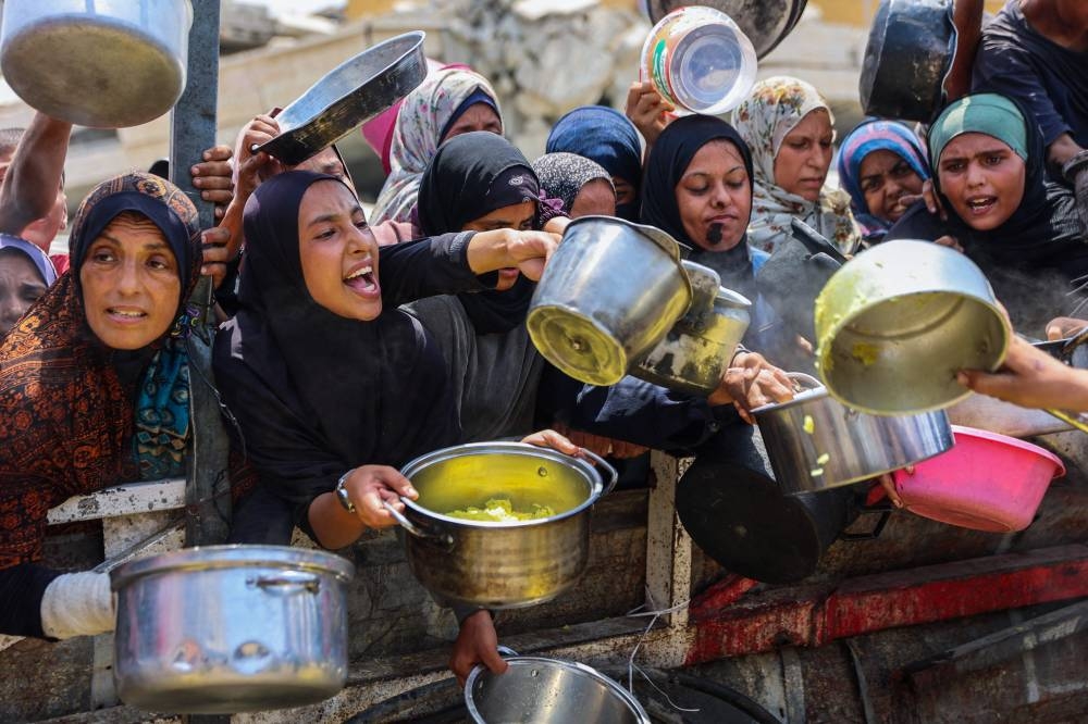 Palestinians gather to receive cooked meals from a food distribution center in Gaza City on August 13, 2025. (AFP)