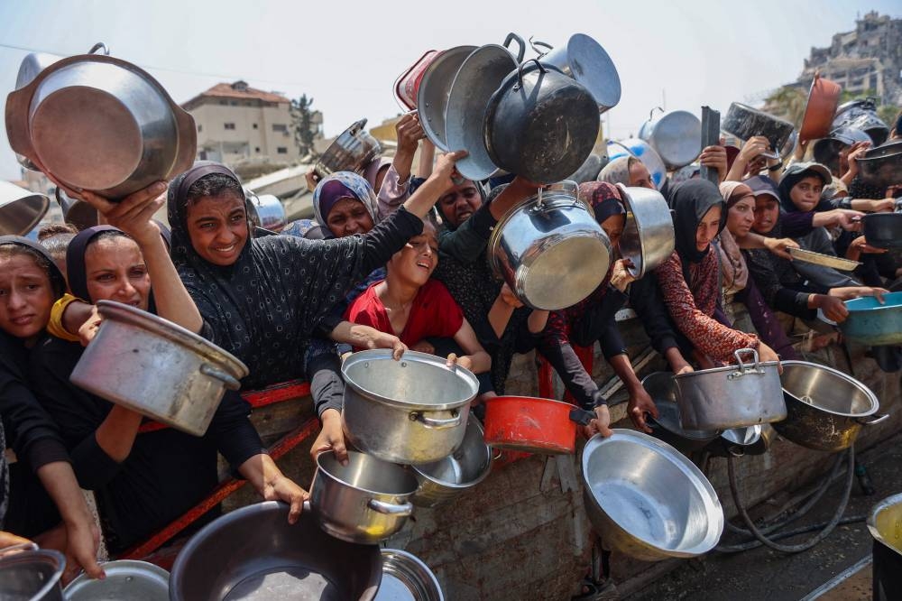Palestinians gather to receive cooked meals from a food distribution center in Gaza City on August 13, 2025. (AFP)