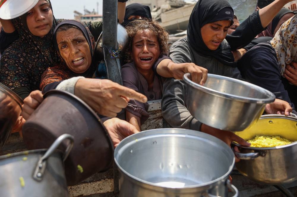 A Palestinian girl cries as she tries to receive cooked meals along with others from a food distribution center in Gaza City on August 13, 2025. (AFP)