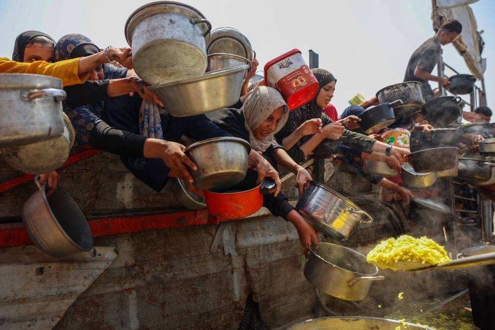 Palestinians gather to receive cooked meals from a food distribution center in Gaza City on August 13, 2025. (AFP)