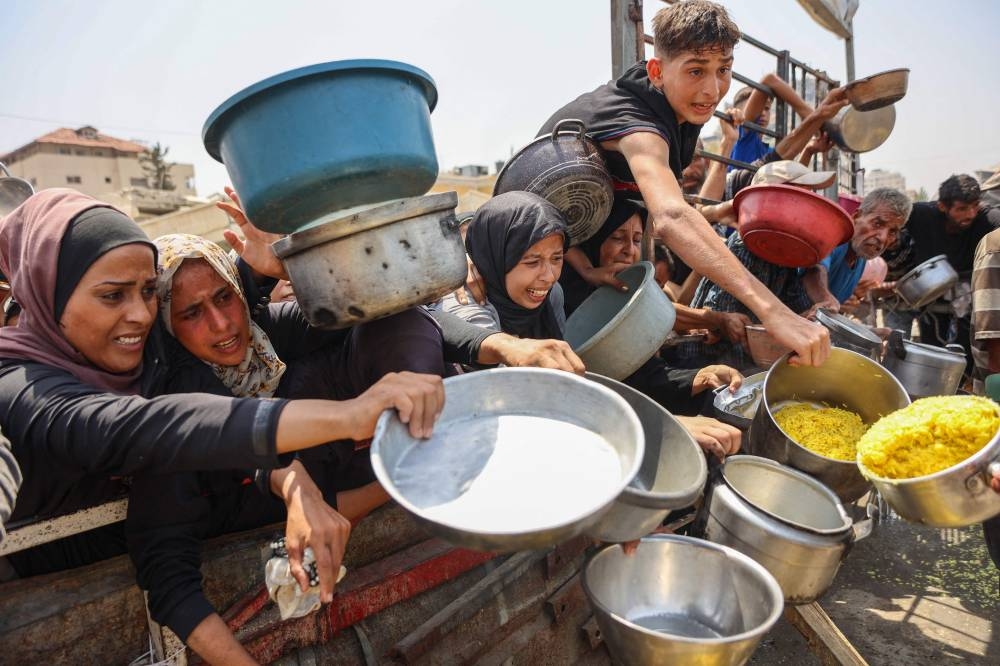 Palestinians gather to receive cooked meals from a food distribution center in Gaza City on August 13, 2025. (AFP)