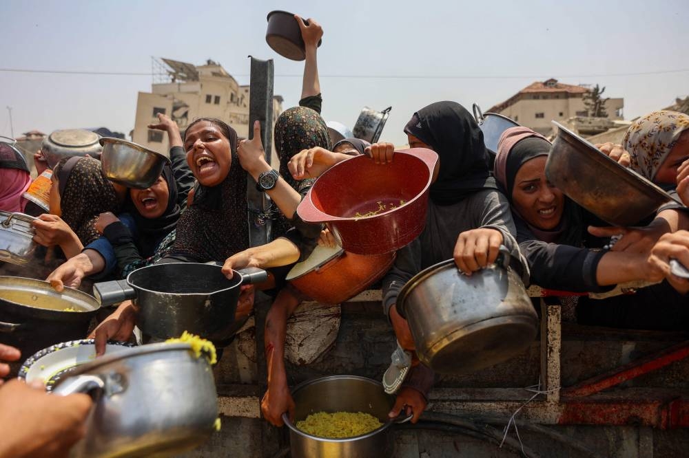 Palestinians gather to receive cooked meals from a food distribution center in Gaza City on August 13, 2025. (AFP)