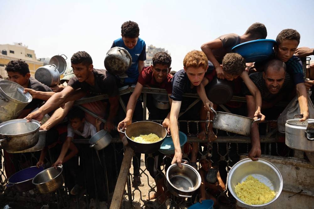 Palestinians gather to receive cooked meals from a food distribution center in Gaza City on August 13, 2025.(AFP)