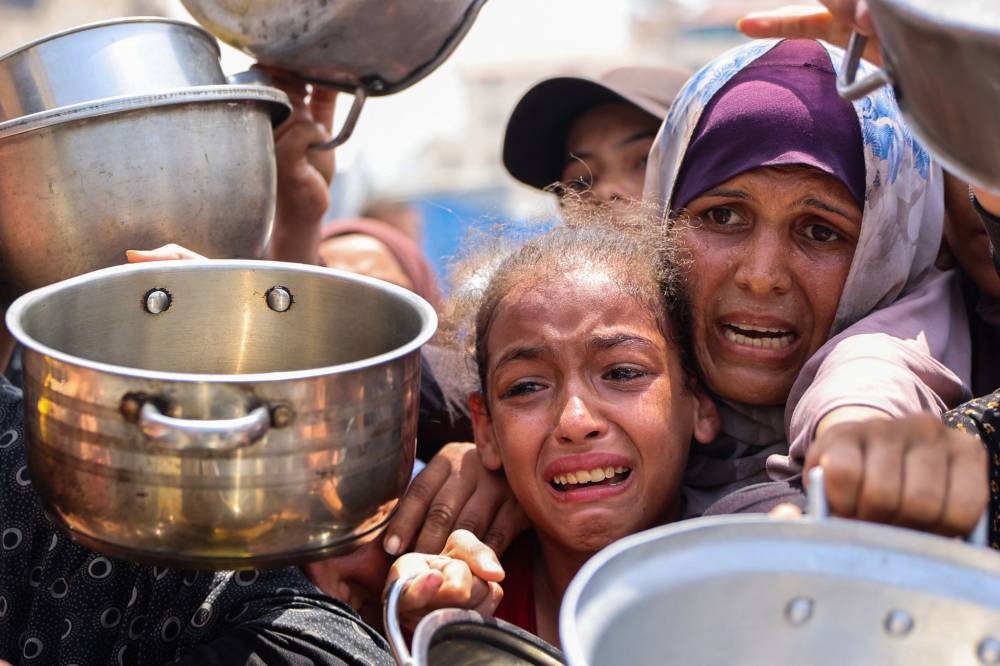 Palestinians gather to receive cooked meals from a food distribution center in Gaza City on August 13, 2025.(AFP)