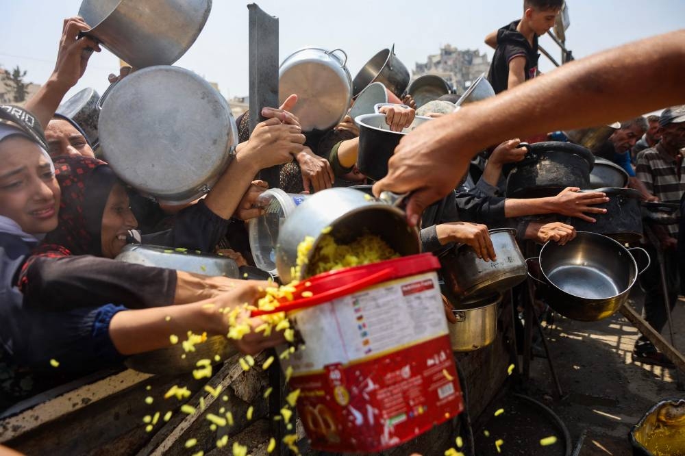 Palestinians gather to receive cooked meals from a food distribution center in Gaza City on August 13, 2025. Israeli military said on August 13 it had approved the framework for a new offensive in the Gaza Strip, as Hamas condemned what it called "aggressive" Israeli ground incursions in Gaza City. The approval for the expanded offensive comes days after Israel's security cabinet called for the seizure of Gaza's largest city, following 22 months of war that have created dire humanitarian conditions in the Palestinian territory. (AFP)