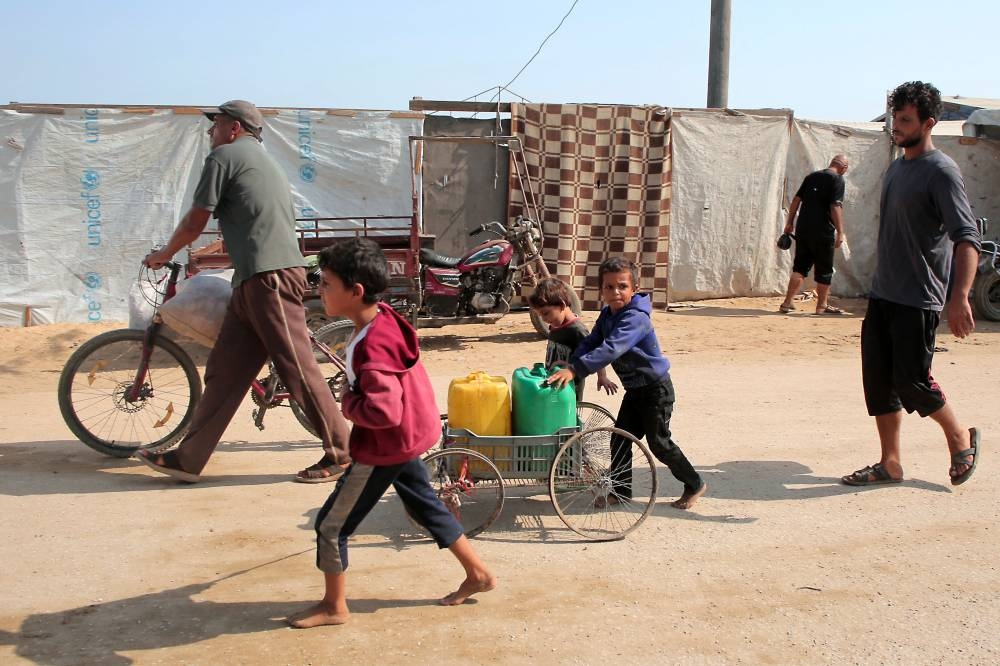 Displaced Palestinians transport water containers in the Mawasi area of Khan Yunis, on August 14, 2025, (AFP)