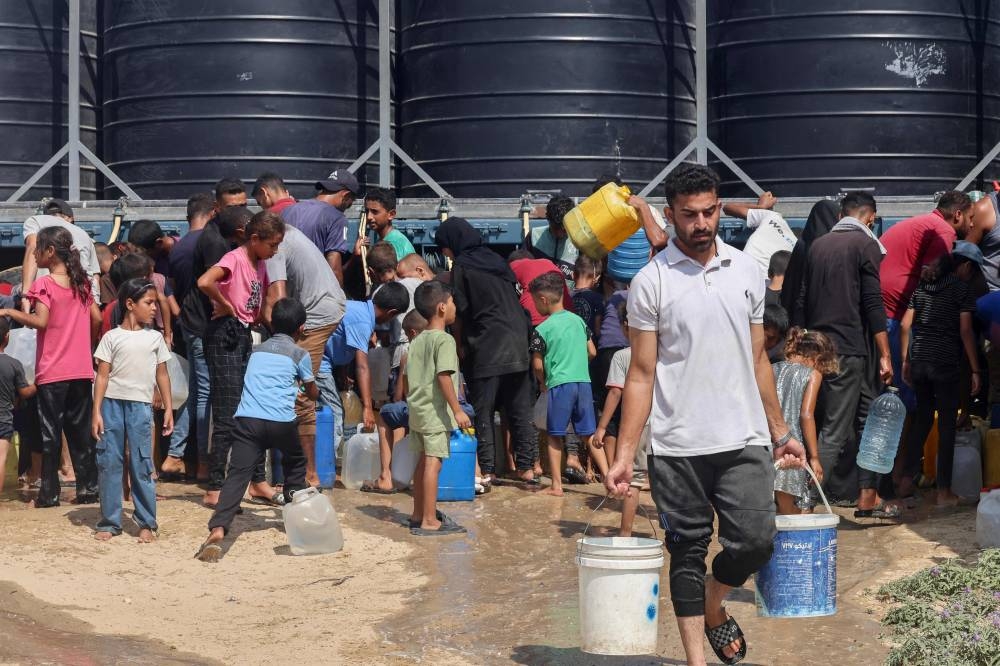 Displaced Palestinians fill water containers in the Mawasi area of Khan Yunis, on August 14, 2025 (AFP)