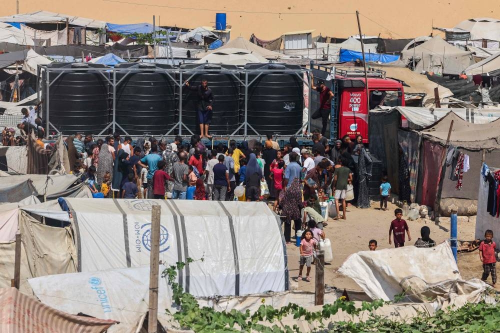 Displaced Palestinians attempt to fill water tanks in the Mawasi area of Khan Yunis, on August 14, 2025 (AFP)