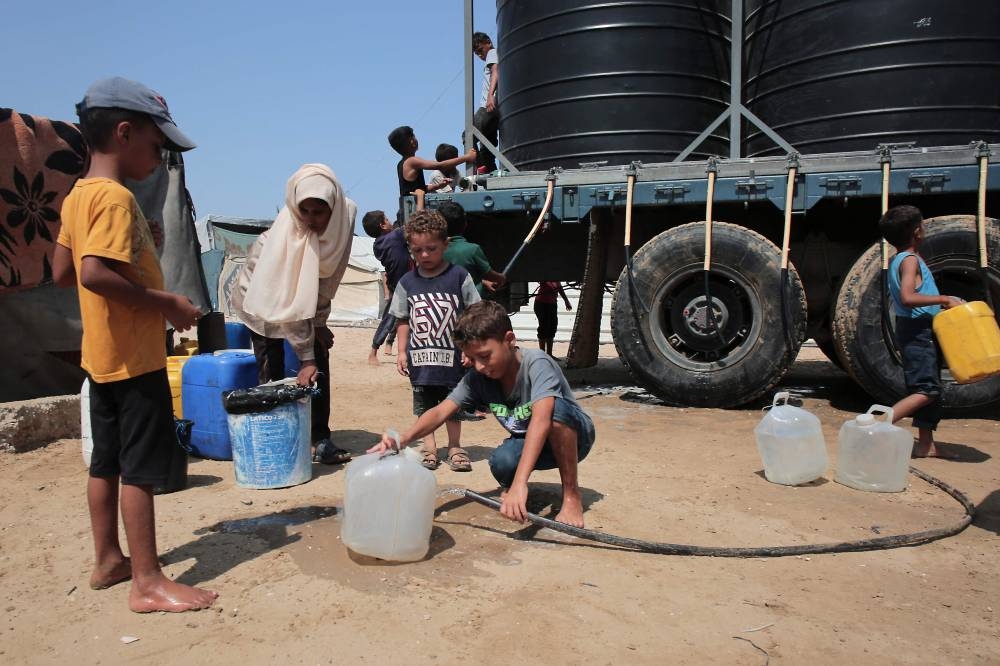 Displaced Palestinians fill water containers in the Mawasi area of Khan Yunis, on August 14, 2025(AFP)