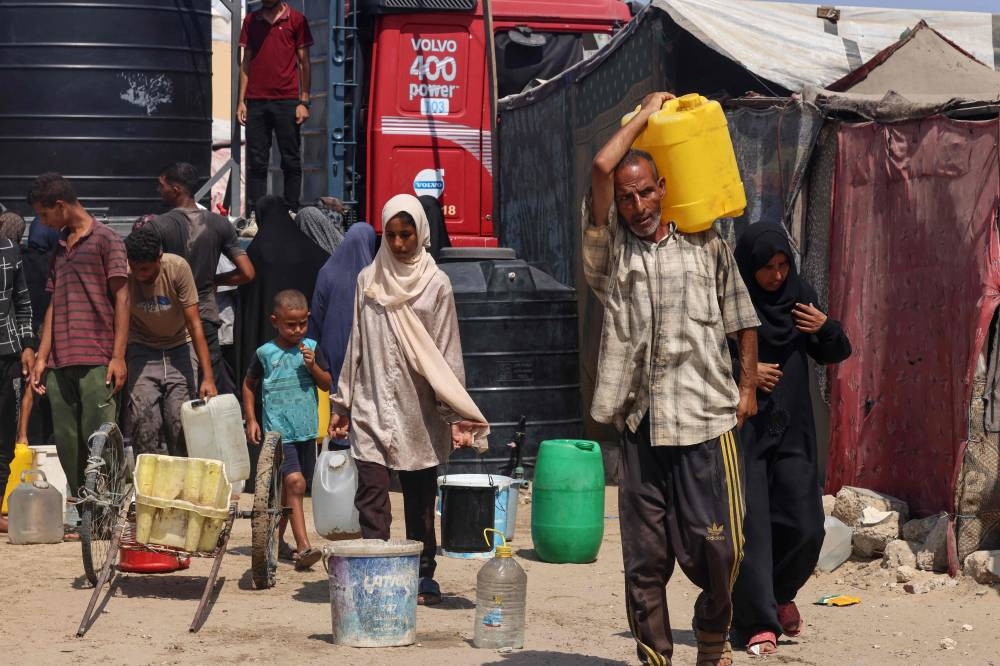 Displaced Palestinians fill water containers in the Mawasi area of Khan Yunis, on August 14, 2025 (AFP)
