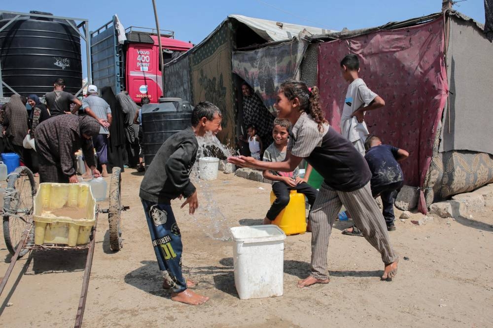 A girl splashes water on a boy as displaced Palestinians gather to fill water containers in the Mawasi area of Khan Yunis, on August 14, 2025 (AFP)