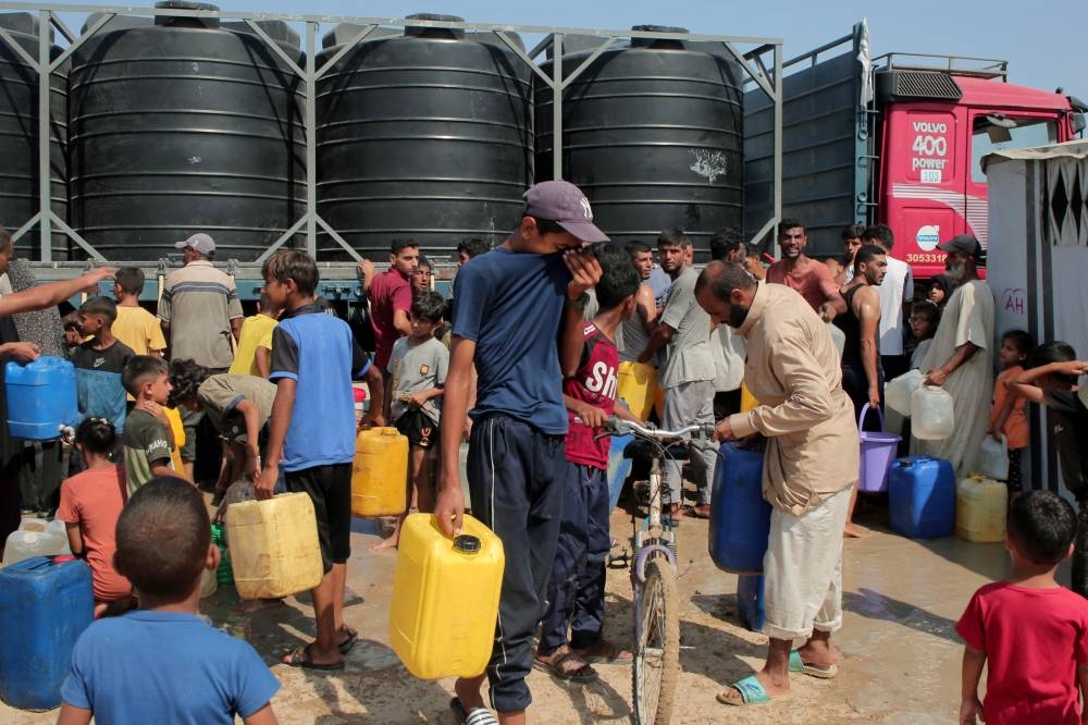 Displaced Palestinians attempt to fill water containers in the Mawasi area of Khan Yunis, on August 14, 2025 (AFP)