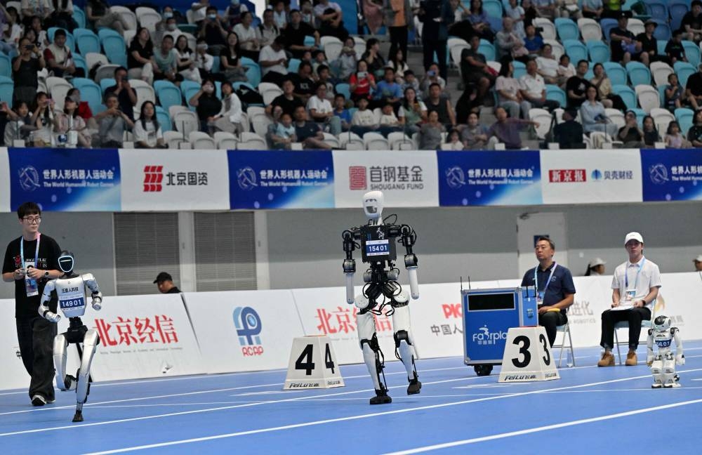 Engineers follow their robots competing in the 100M run during the World Humanoid robots games in Beijing on August 16, 2025. (AFP)