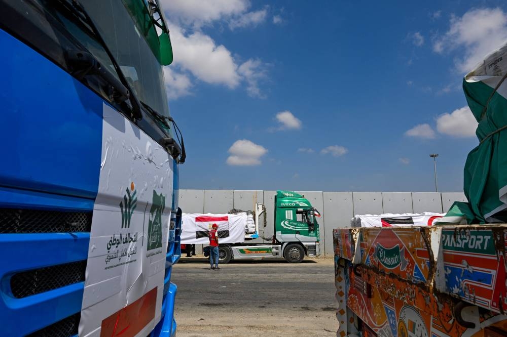 A man walks past trucks loaded with aid for Gaza, waiting on the Egyptian side of the Rafah crossing in Rafah on August 18, 2025. Rights group Amnesty International on August 18 accused Israel of enacting a "deliberate policy" of starvation in Gaza, as the United Nations and aid groups warn of famine in the Palestinian territory. Israel, while heavily restricting aid allowed into the Gaza Strip, has repeatedly rejected claims of deliberate starvation in the 22-month-old war. (AFP)