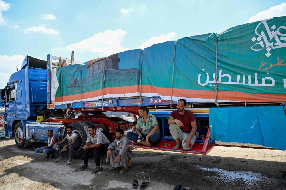 Drivers wait beside a truck loaded with aid for Gaza on the Egyptian side of the Rafah crossing in Rafah on August 18, 2025. Rights group Amnesty International on August 18 accused Israel of enacting a "deliberate policy" of starvation in Gaza, as the United Nations and aid groups warn of famine in the Palestinian territory. Israel, while heavily restricting aid allowed into the Gaza Strip, has repeatedly rejected claims of deliberate starvation in the 22-month-old war. (AFP)