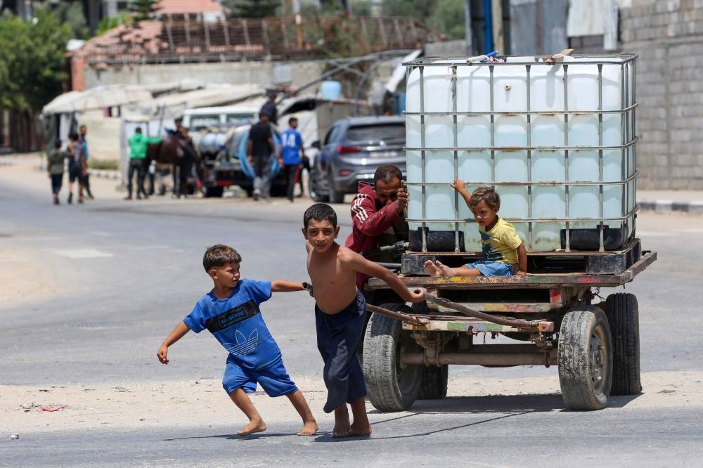 A man and young children push on a cart carrying a water tank at the Bureij camp for displaced Palestinians in the central Gaza Strip, on August 17, 2025. After more than 22 months of war, UN-backed experts have warned of widespread famine unfolding in Gaza, where Israel has drastically curtailed the amount of humanitarian aid it allows in and convoys have been repeatedly looted. (AFP)
