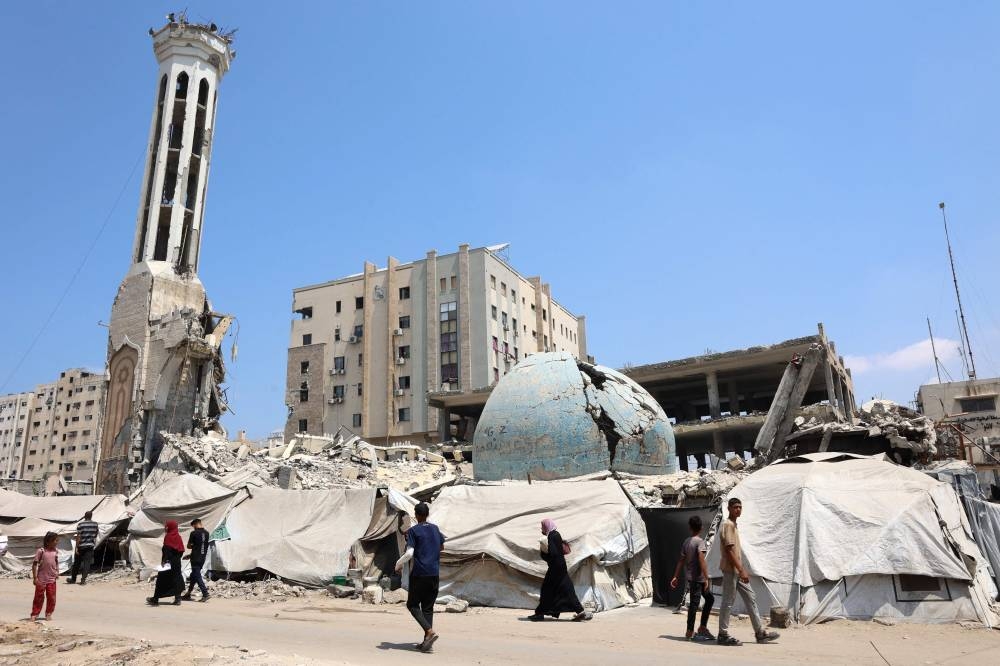 Palestinians walk past the destroyed Abu Khudra Mosque in Gaza City on August 18, 2025. (AFP)