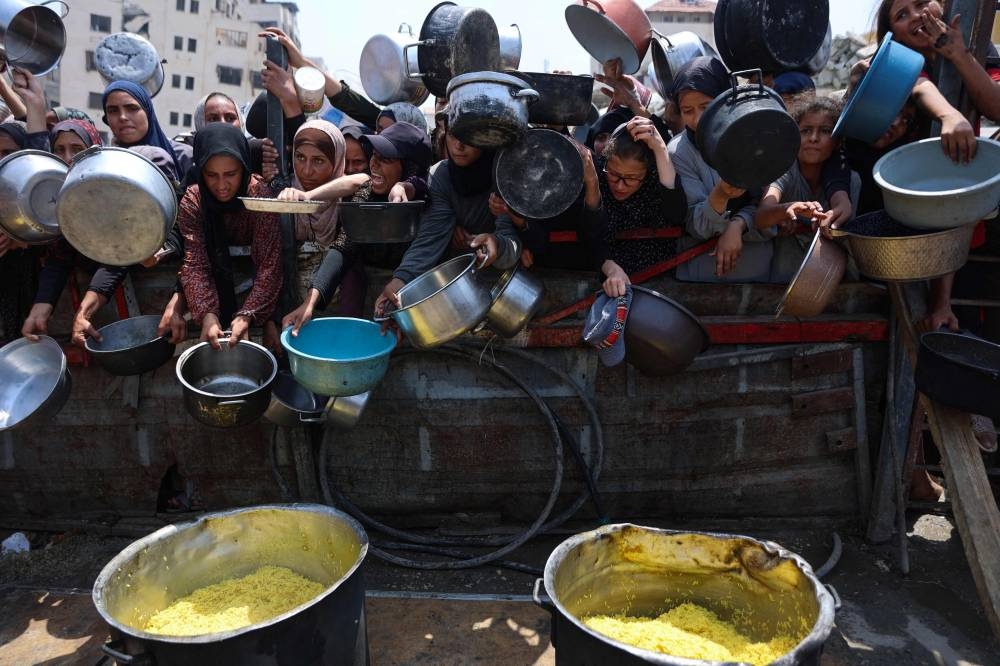 Palestinians gather to receive cooked meals from a food distribution center in Gaza City on August 13, 2025. (AFP)