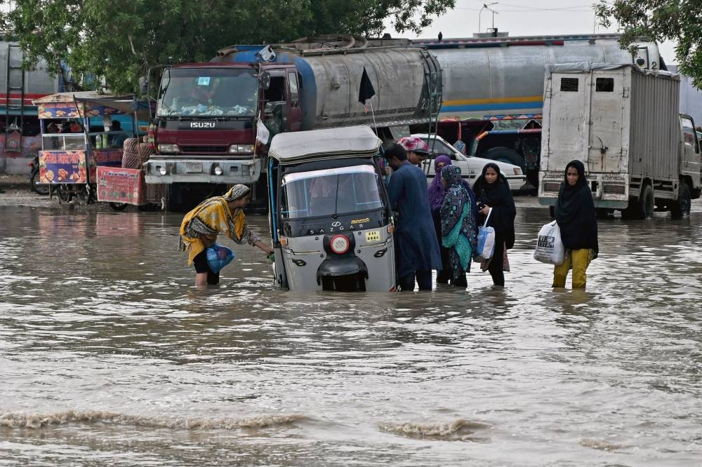Passengers disembark from an auto rickshaw that got stranded on a flooded road after heavy monsoon rains in Karachi Wednesday.