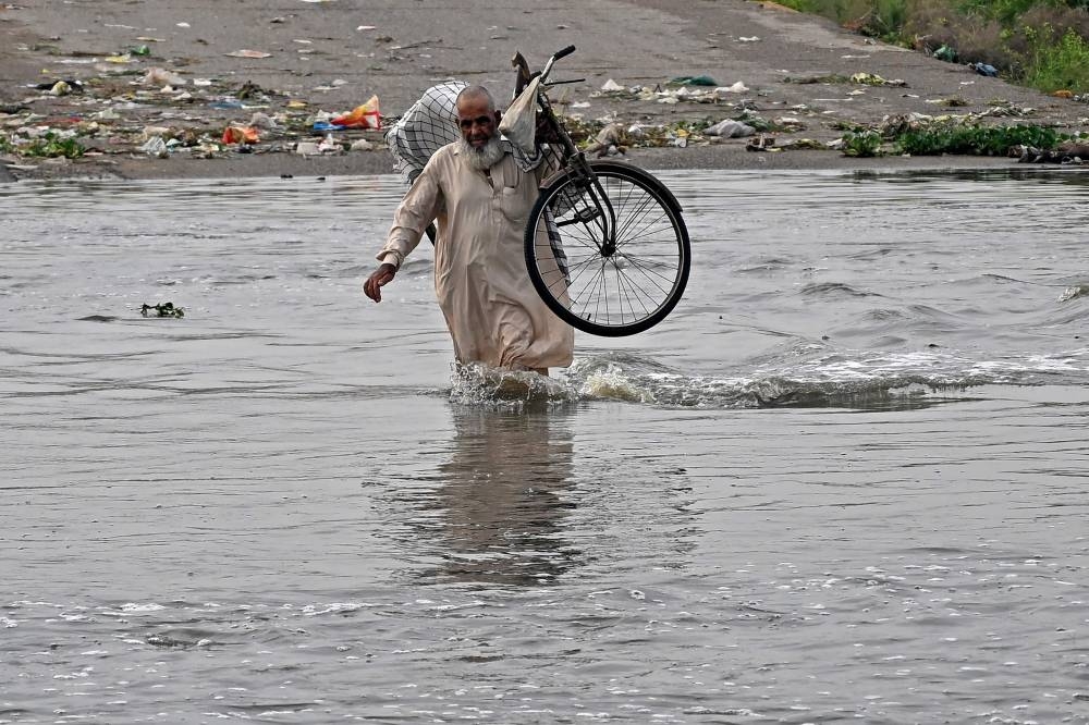 A man carries his bicycle as he wades along a flooded road after heavy monsoon rains in Karachi on August 20, 2025. (AFP)